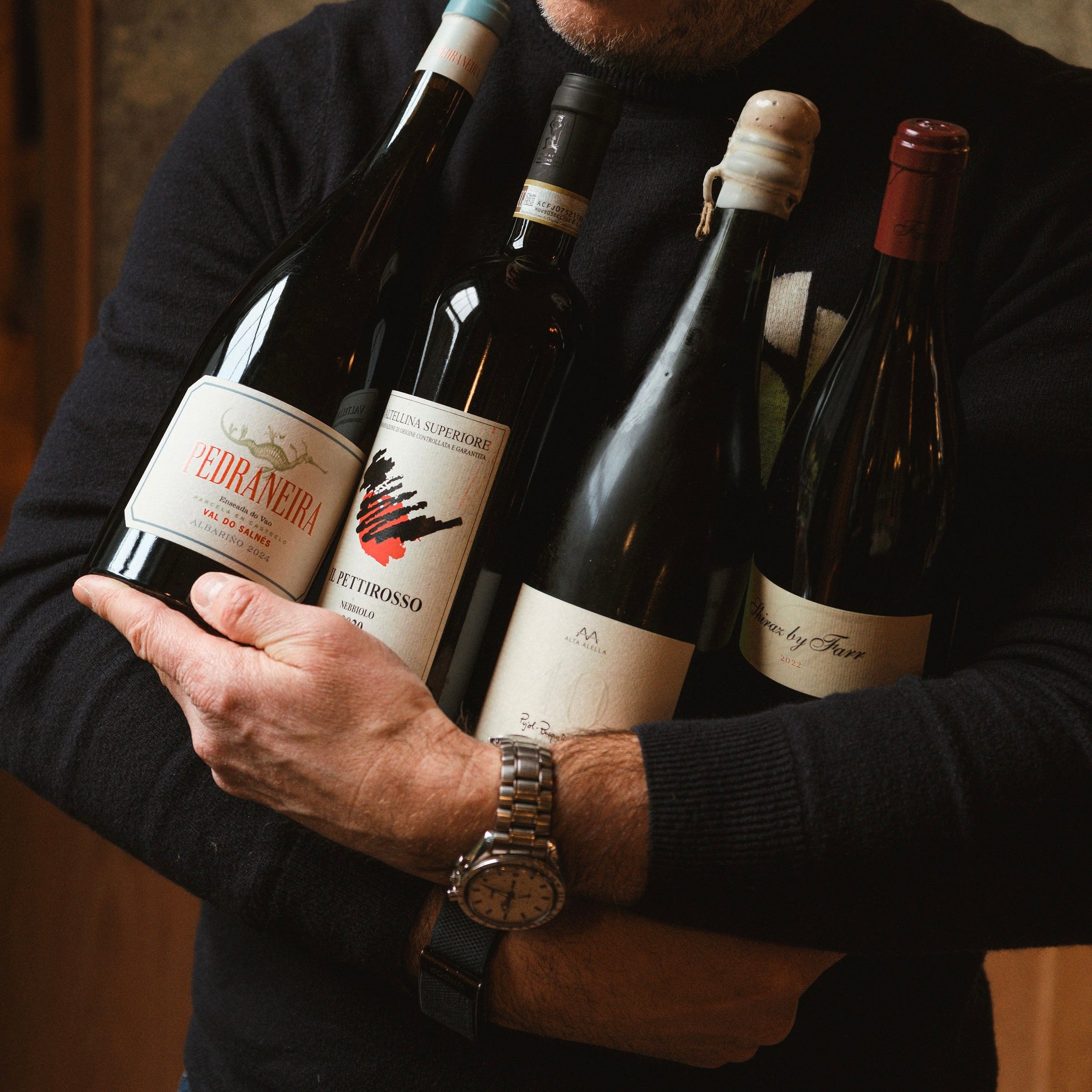 Man holding four bottles of wine with visible labels.